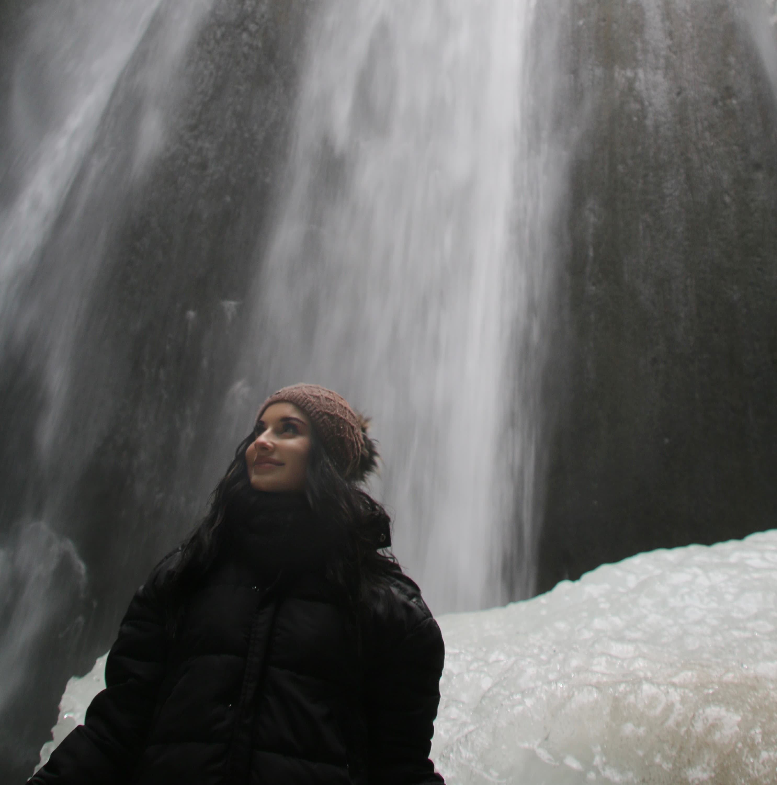 Person steht vor einem Wasserfall in einer winterlichen Umgebung, umgeben von Eis und Gestein.