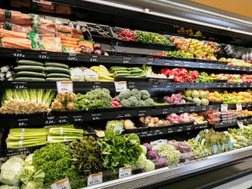 Bunte Auswahl an frischem Gemüse und Obst im Supermarkt, sortiert in Regalen.