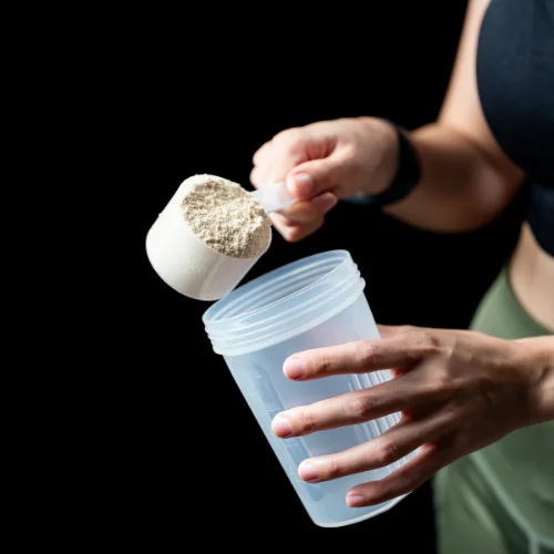 Person, die einen Messlöffel mit Proteinpulver in einen Shaker füllt.